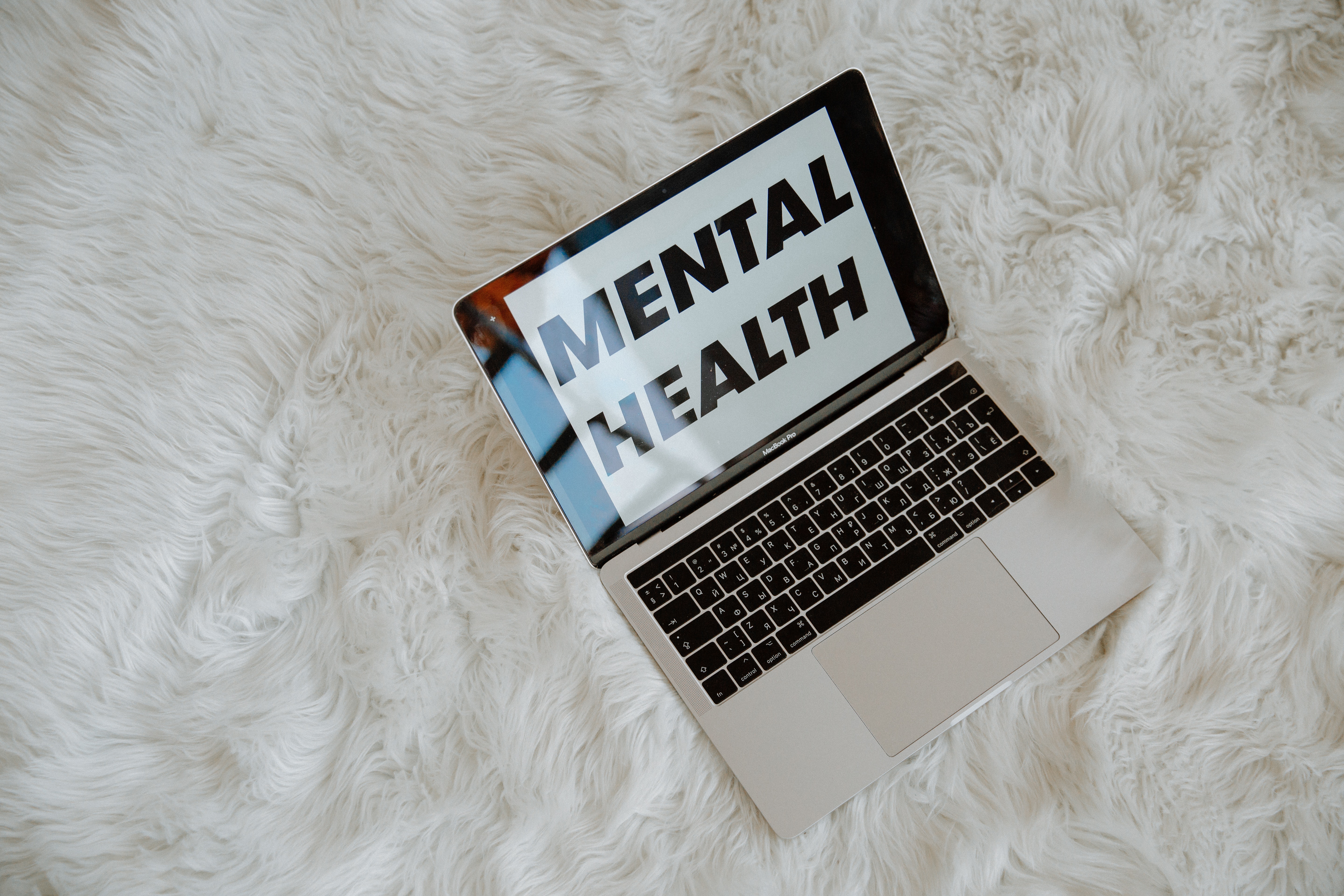 A computer sits on a bed, whose screen has two words on it — mental health.